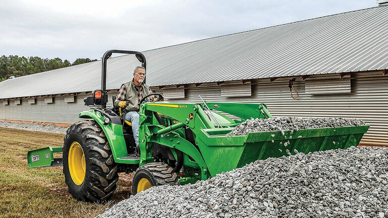person operating a 4066m using loader to lift gravel with a barn in the background