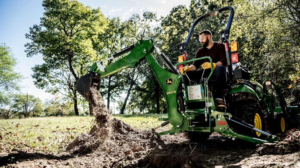 person operating 260b backhoe on back of compact utility tractor