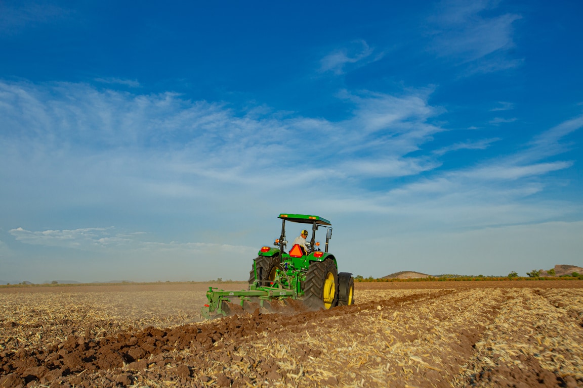 Tractor John Deere en el campo, visto de espaldas, con un cielo azul