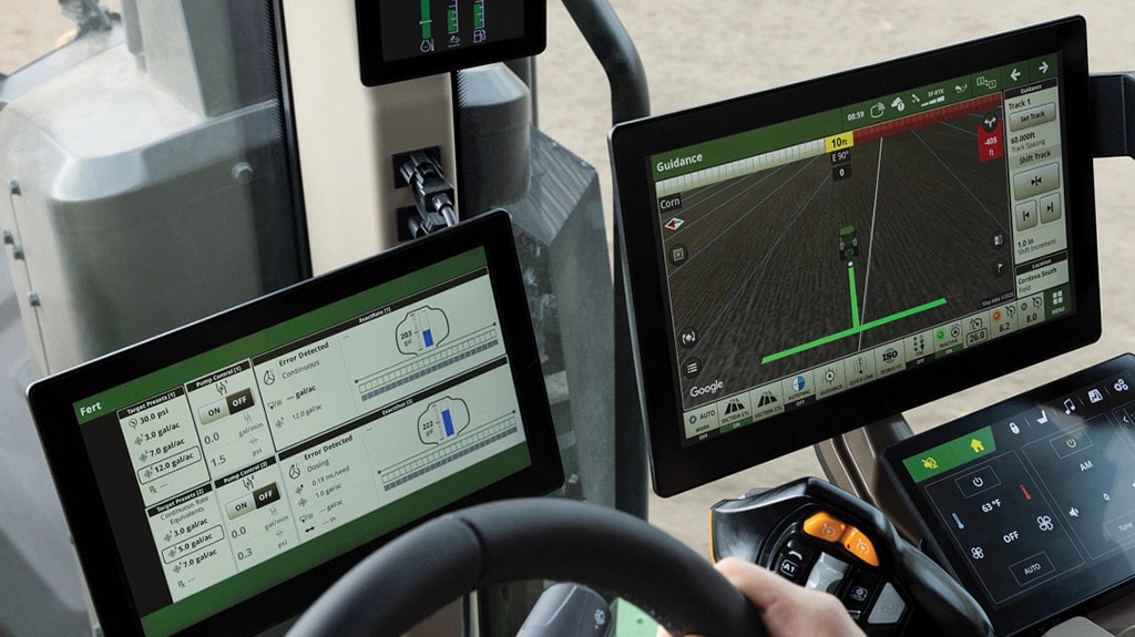 Tractor cab interior with multiple digital displays showing guidance maps and machine controls.