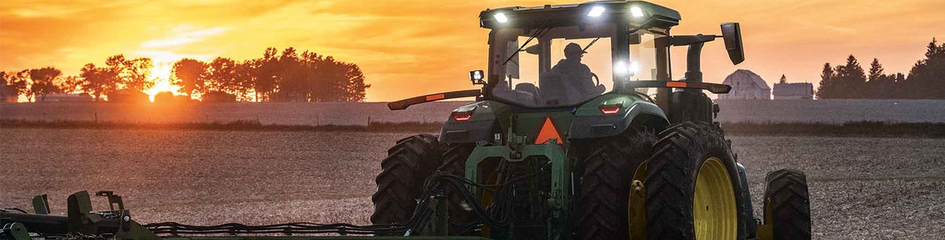 A John Deere 8 Series Row Crop tractor in a field at sunset.