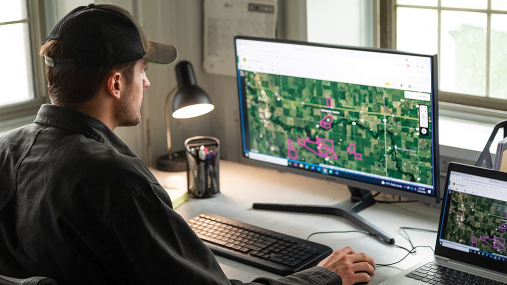 Man sitting at desk in front of a computer display, working in John Deere Operations Center. Man sitting at desk in front of a computer display, working in John Deere Operations Center.