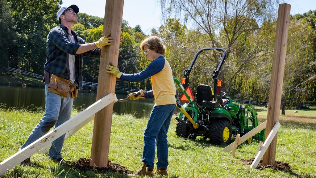 Man and woman installing fence posts in a pasture with a 1 series tractor in the background