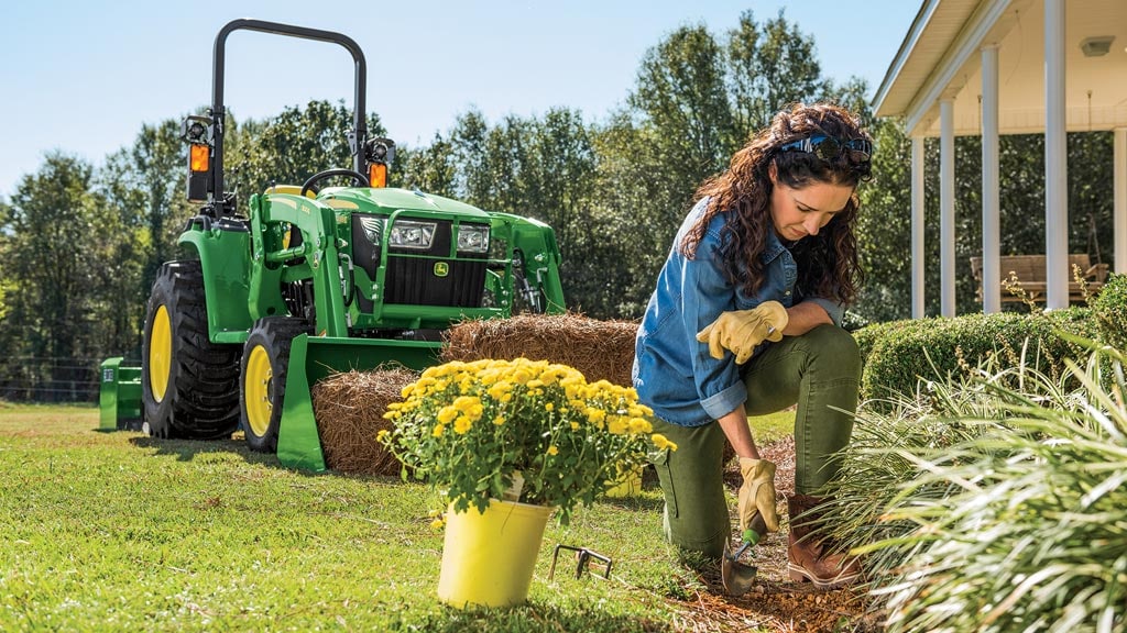 woman working in a flower bed with 3 series tractor in the background