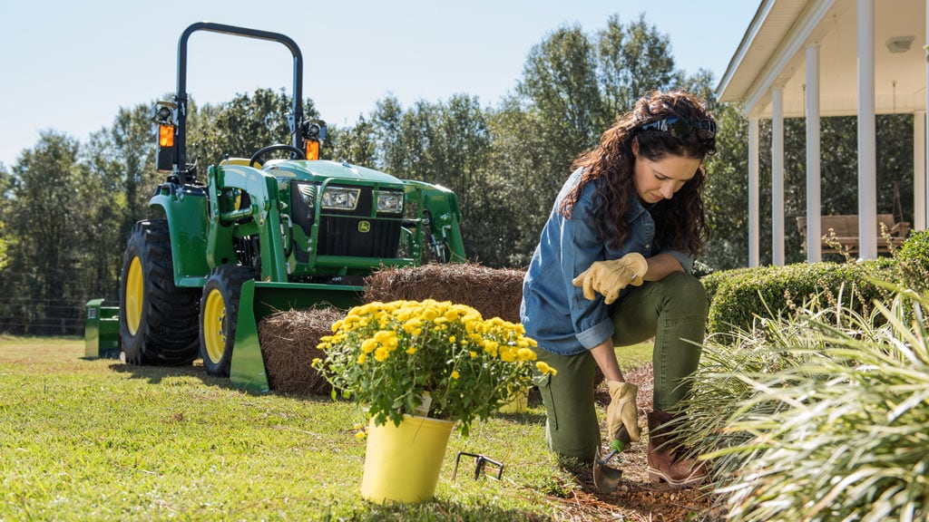 Woman working on flower bed with a 3e tractor in the background