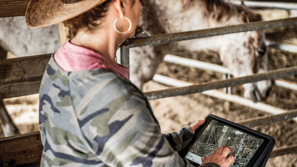 woman in horse stable operating JDLink on wireless tablet