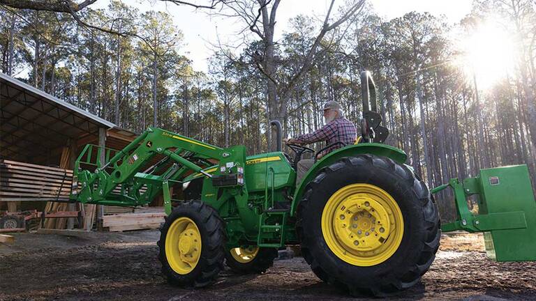 A pallet fork attachment is used by a green tractor to move planks under an open storage area.