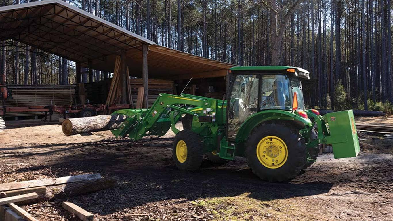 A grapple attachment is used by a green tractor to move logs under an open storage area.