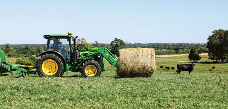 5M tractor moving a hay bail in a cow pasture