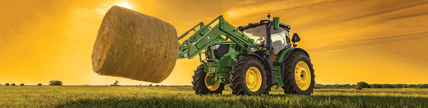 6M 125 Tractor with loader lifting a hay bale during sunset