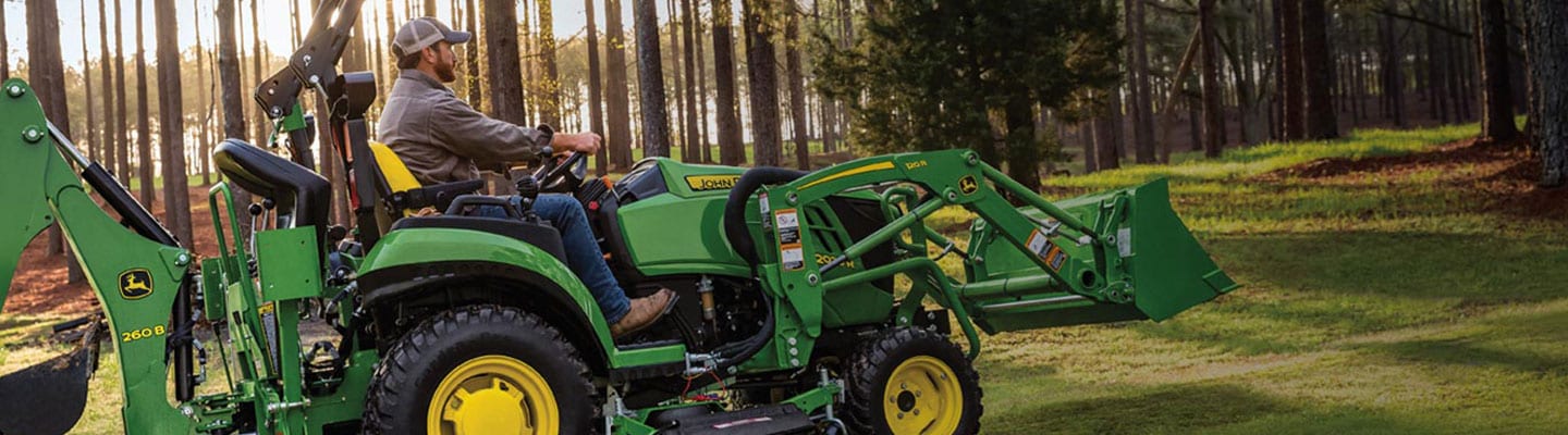 person riding a compact tractor in a forest