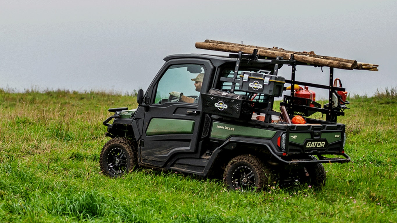 A HVAC cabbed olive-green Gator carries a load of timber on a rack along with a cargo box full of tools and supplies.