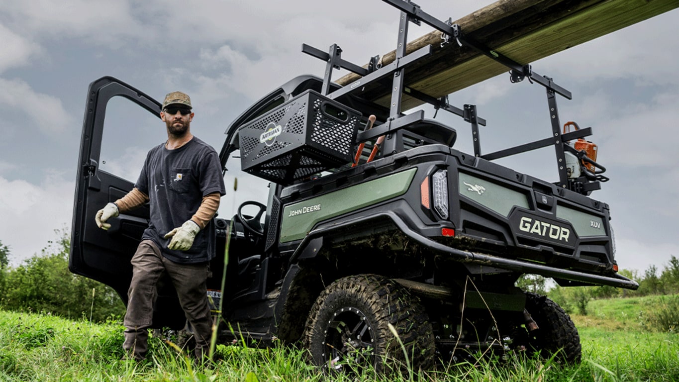 A HVAC cabbed olive-green Gator carrying timber and tools on the racks over its cargo box.