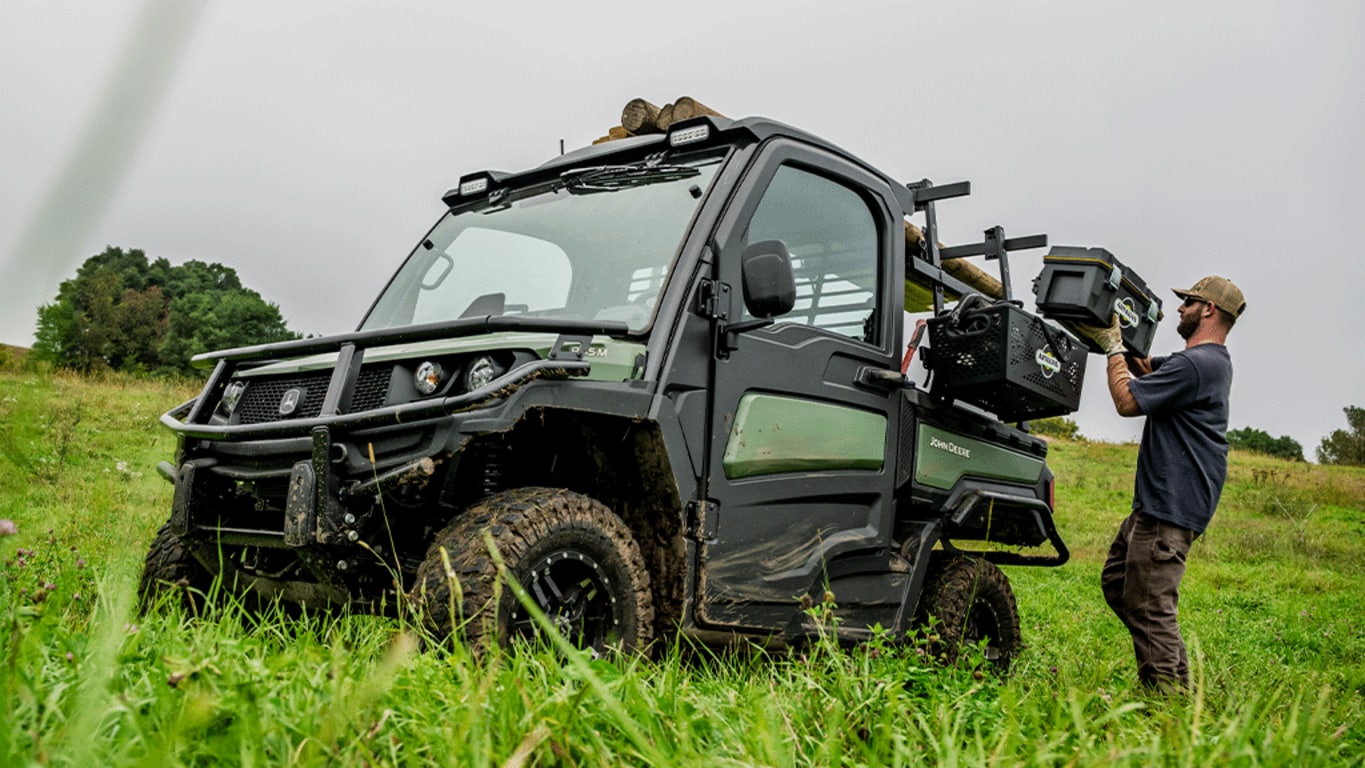 A toolbox is loaded onto the side rack of an olive-green Gator.