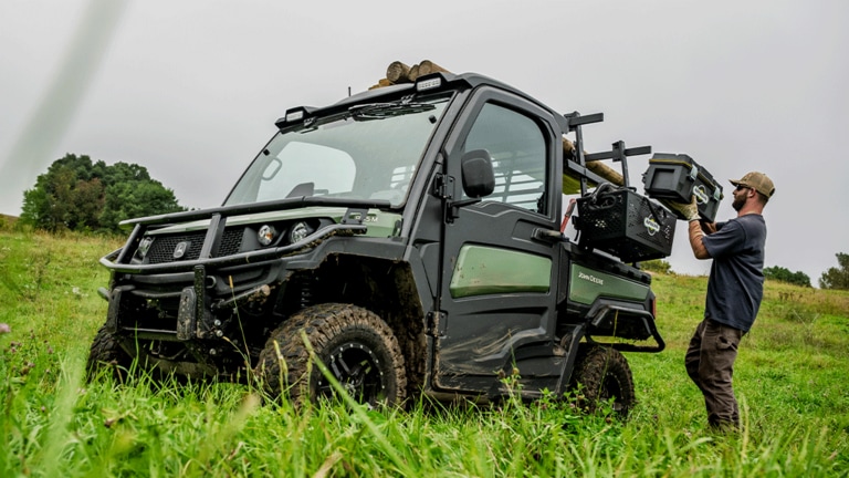 A toolbox is loaded onto the side rack of an olive-green Gator.