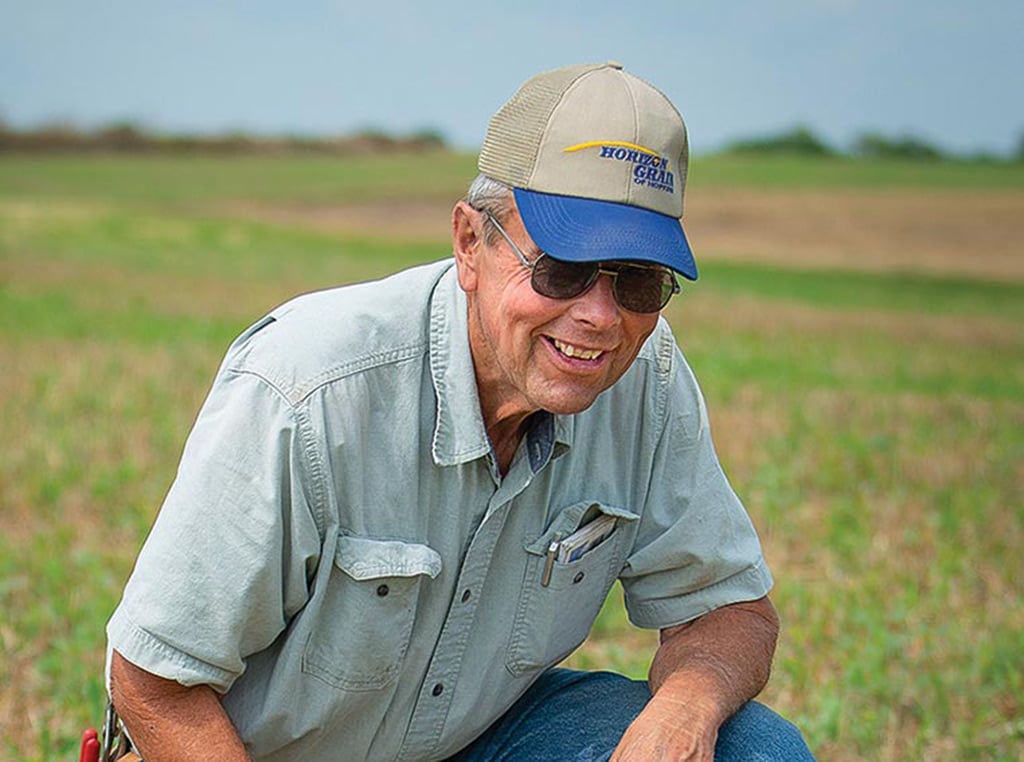 Paul Ackley smiles, kneeling in field