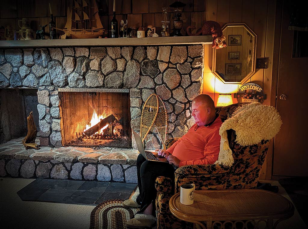 Asmussen sitting by a fireplace with his laptop