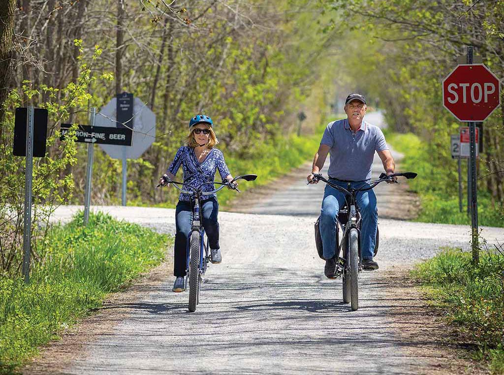 two people riding electric bicycles down a tree-lined-street