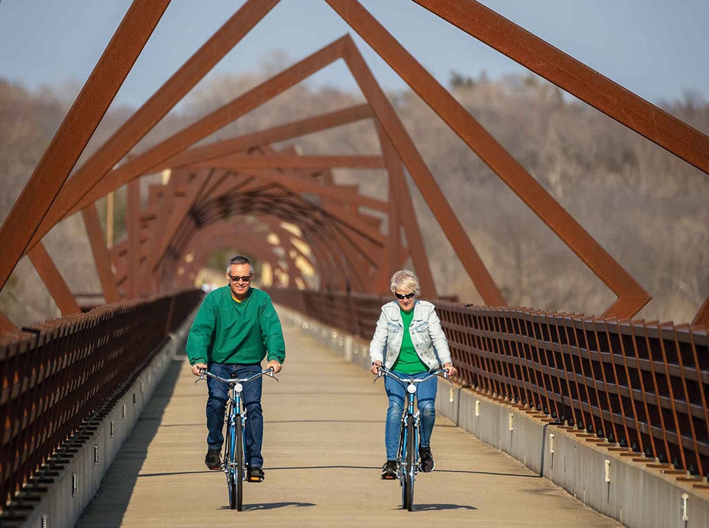man and woman riding bike on bridge with angular installation art tunnel