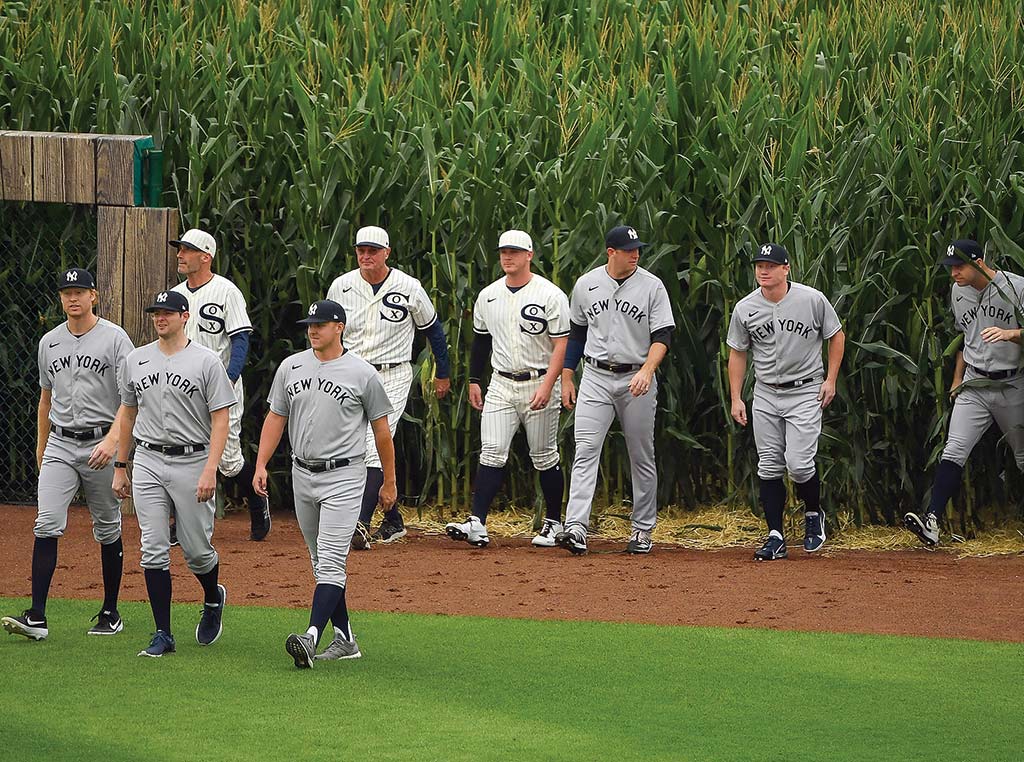 baseball players walking onto the field with corn in the background.