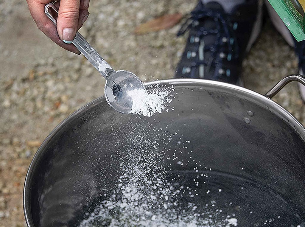 spooning pickling lime powder into pot of water