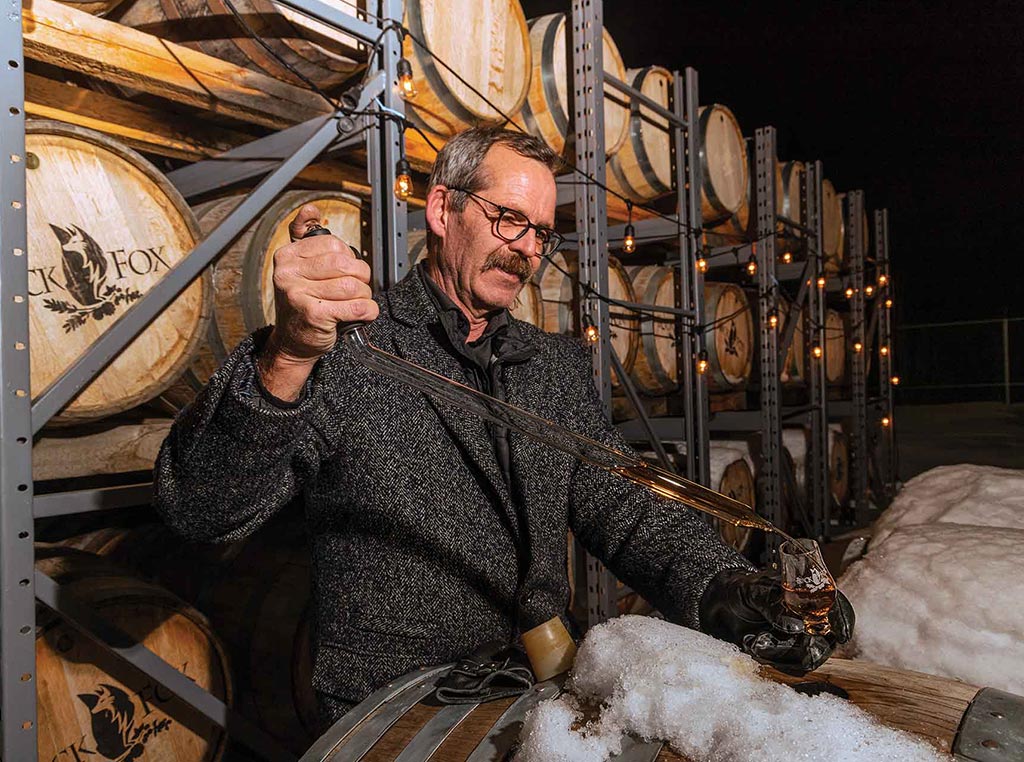 man pouring whisky into tasting glass over barrel