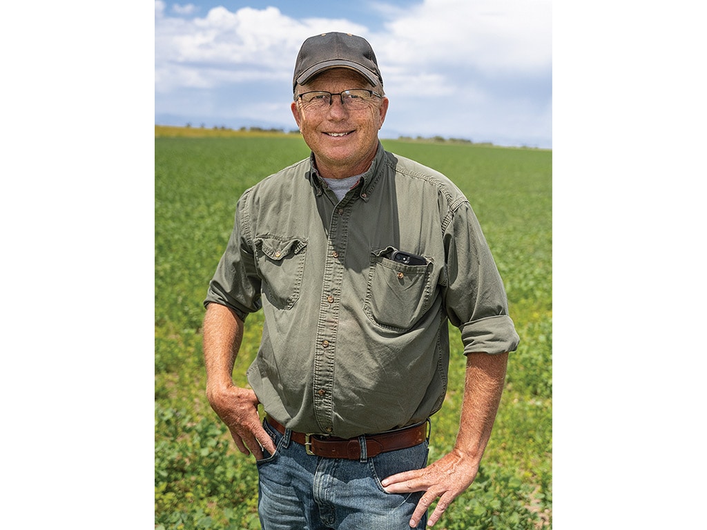 smiling farmer with baseball cap and glasses standing in field