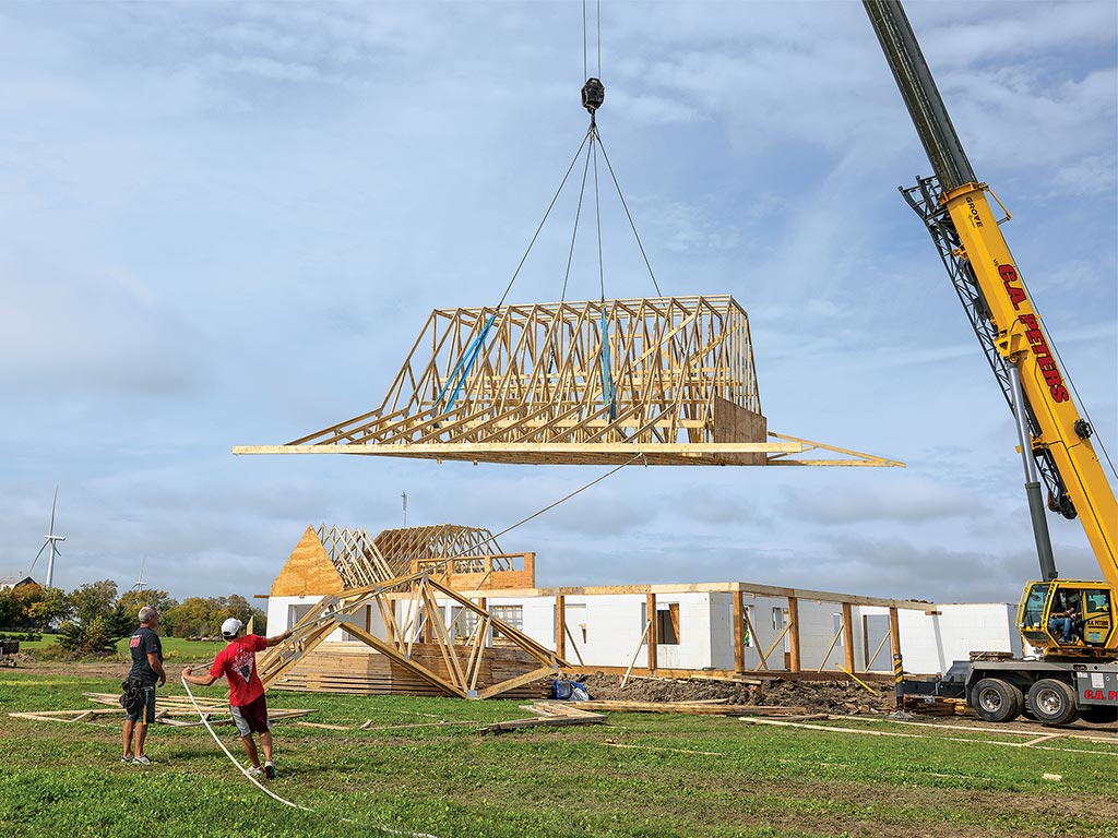  frame of the roof of a house being lifted by a crane with people standing by assisting