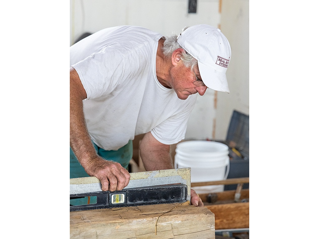 person with white hair and baseball cap on squaring a corner of wood