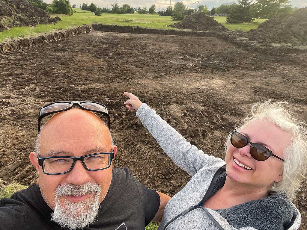 a couple standing on a dirt field smiling with glasses on