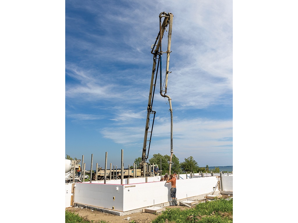  a crane placing a tall vertical pipe with a man guiding it into place