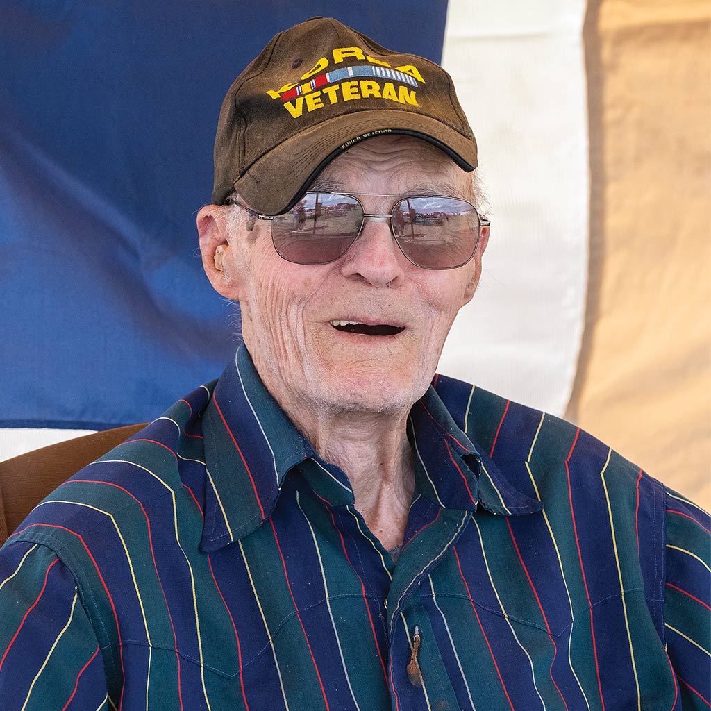  smiling man wearing veterans baseball cap and sunglasses with striped collared shirt