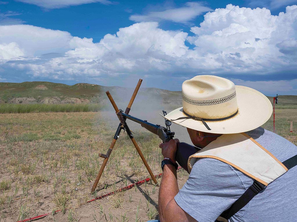 person firing rifle through crisscrossed wooden prop at distant target