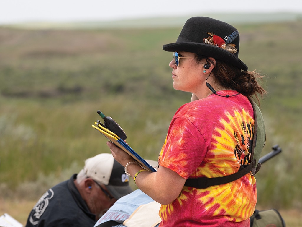 rifle competition scorekeeper with tie died tshirt looking out to field holding yellow legal notepad