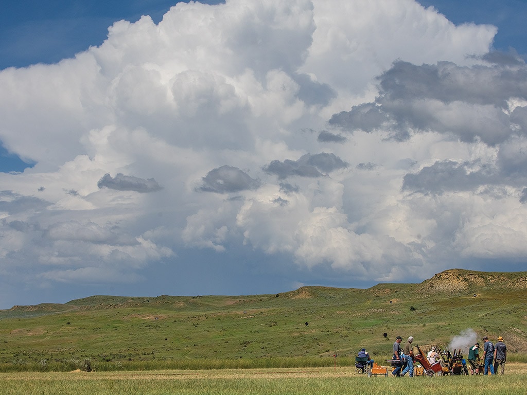 people standing in field with clouds and hills in background