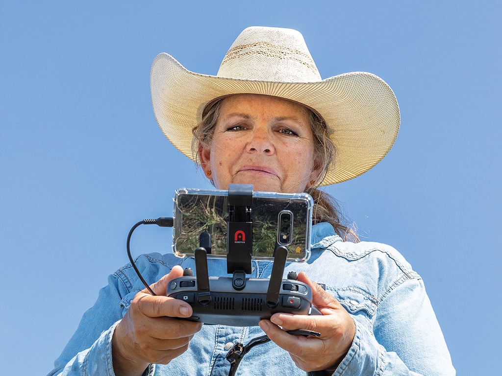 Farmer with cowboy hat on with drone remote plugged into cellphone