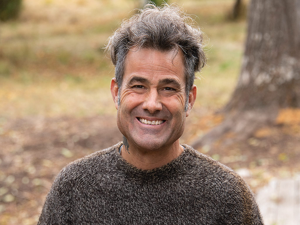  smiling man with knit sweater with trees in the background