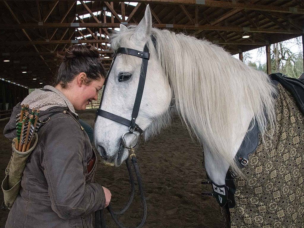 person in a stable leaning into a white horse