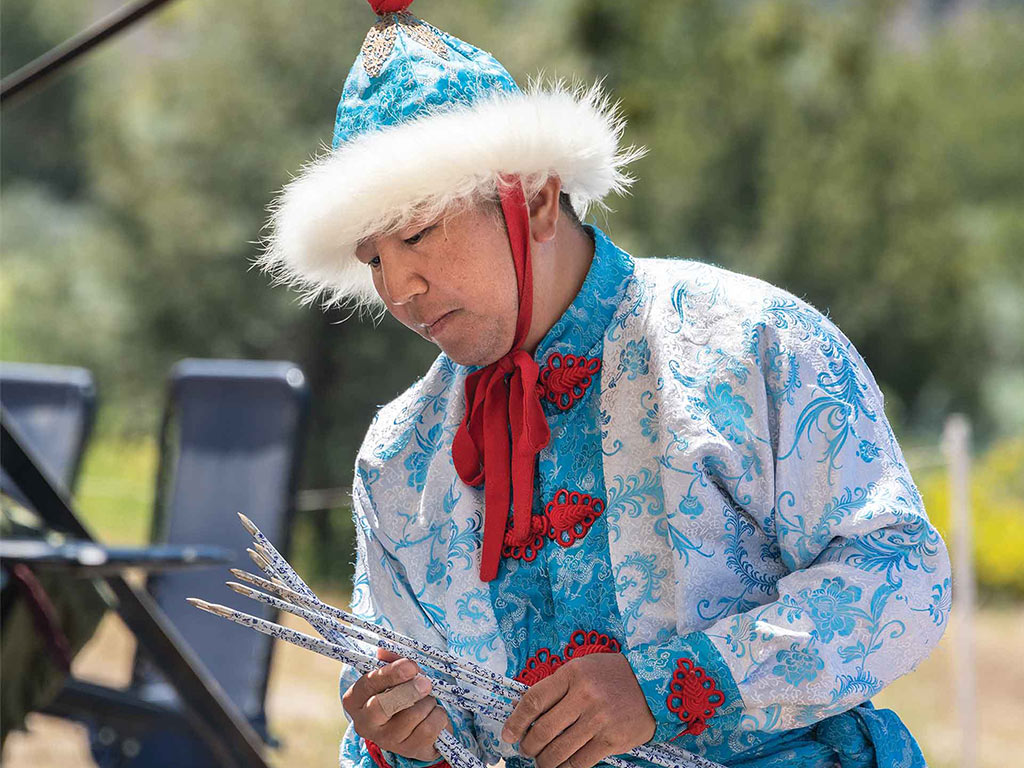 person examining arrows wearing traditional mongolian garb with light blue, white, and red details