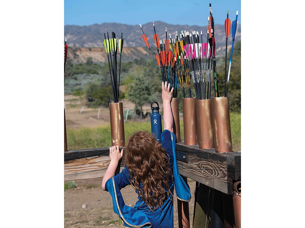 person in a blue dress reaching up to groupings of black arrows with colorful fletchings