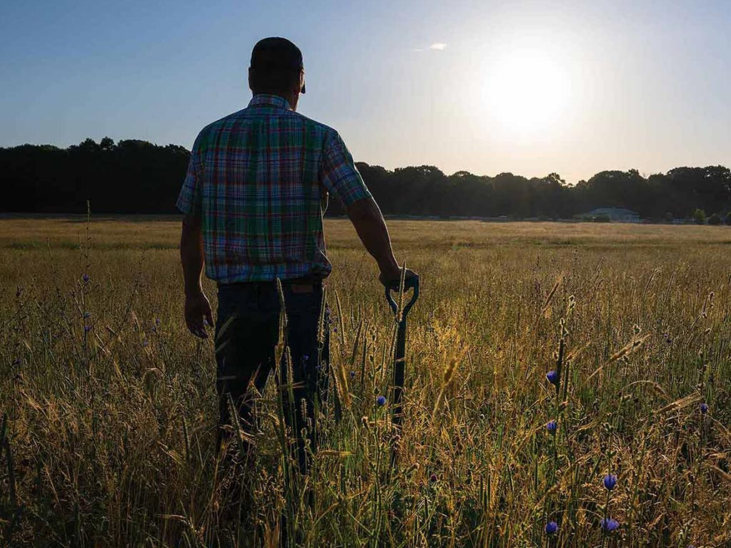 farmer with hand on shovel facing the sun over the horizon