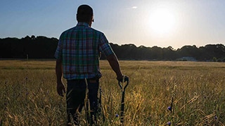 farmer with hand on shovel facing the sun over the horizon