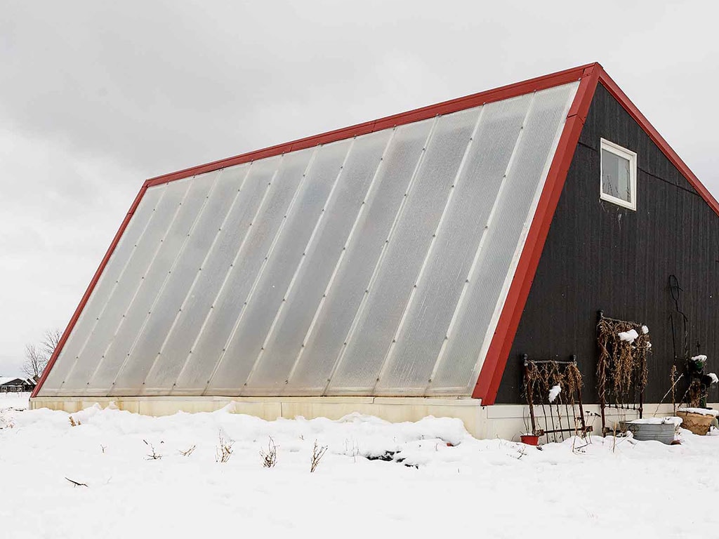 black greenhouse with red trim and translucent white windows surrounded by snow