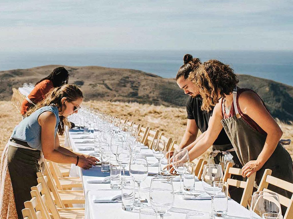 restaurant serving staff setting up long table outside with glasses and napkins