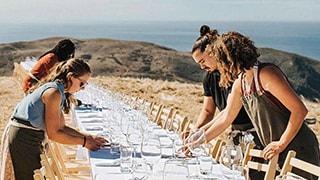 restaurant serving staff setting up long table outside with glasses and napkins