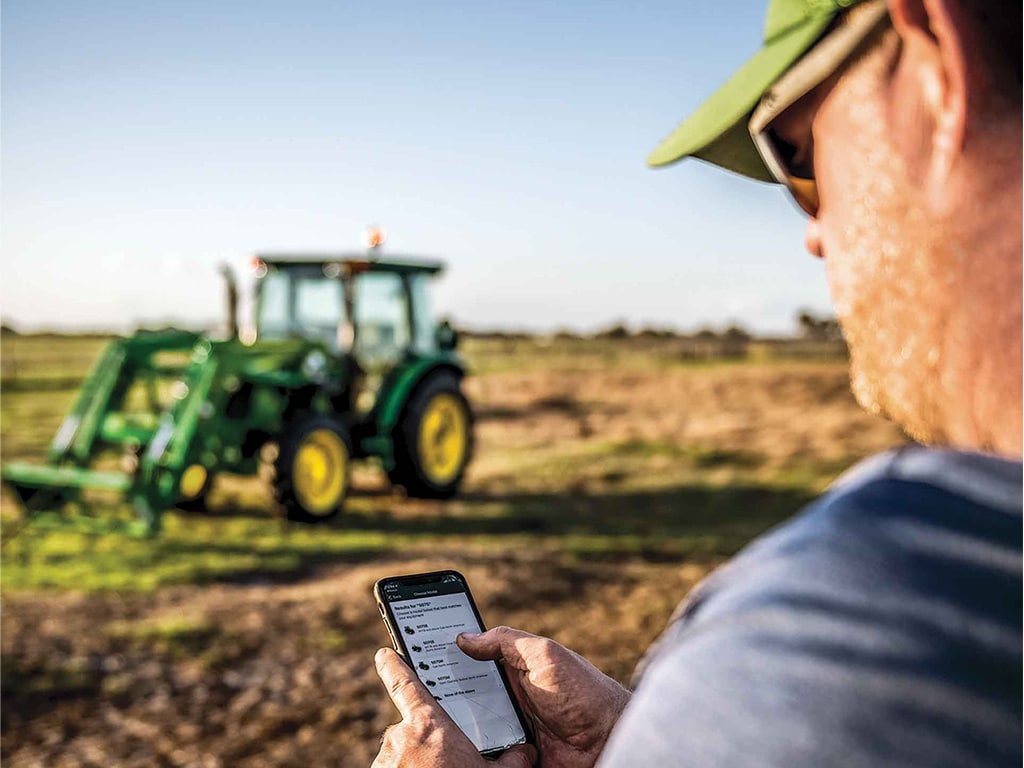 man in field using John Deere Property Center app with tractor in the distance