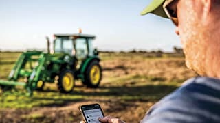 man in field using John Deere Property Center app with tractor in the distance