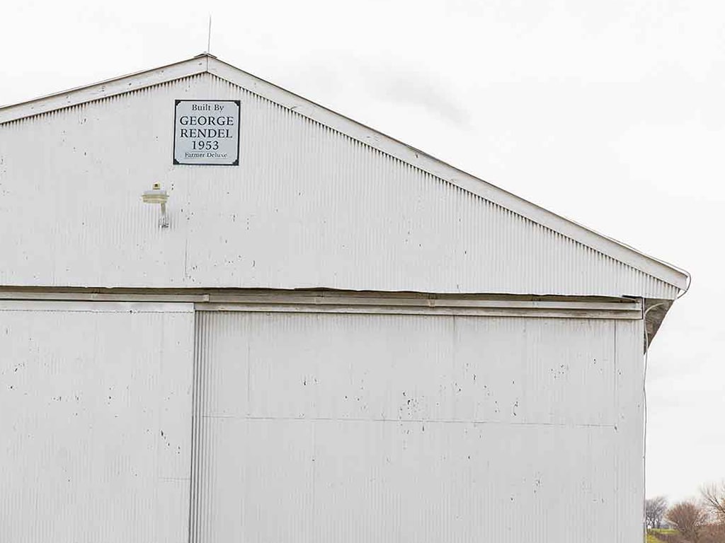 Exterior of view of a white wood panel barn with a plaque at the peak