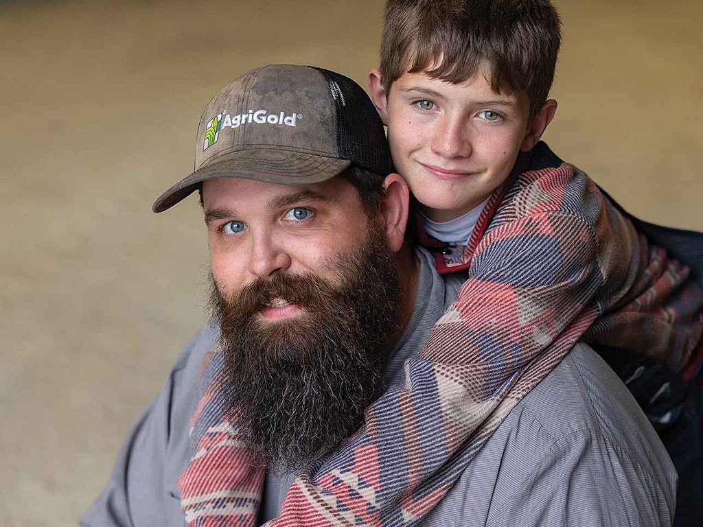 Farmer Zach with son Nate on his back both smiling toward camera
