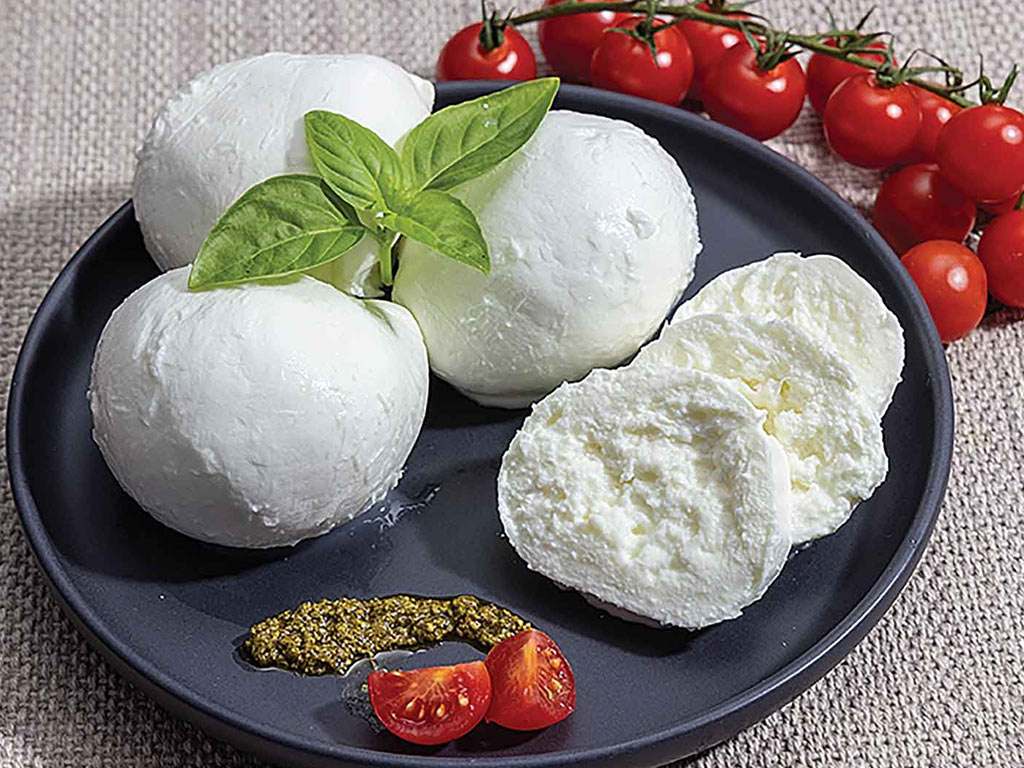 balls and slices of fresh mozzarella cheese on a plate surrounded by red cherry tomatoes 